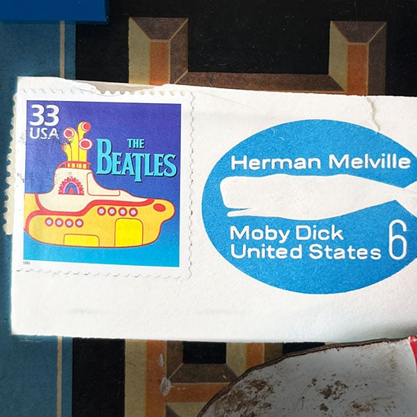 Closeup of a 'The Beatles' and Herman Melville United States postage stamps torn from a letter.