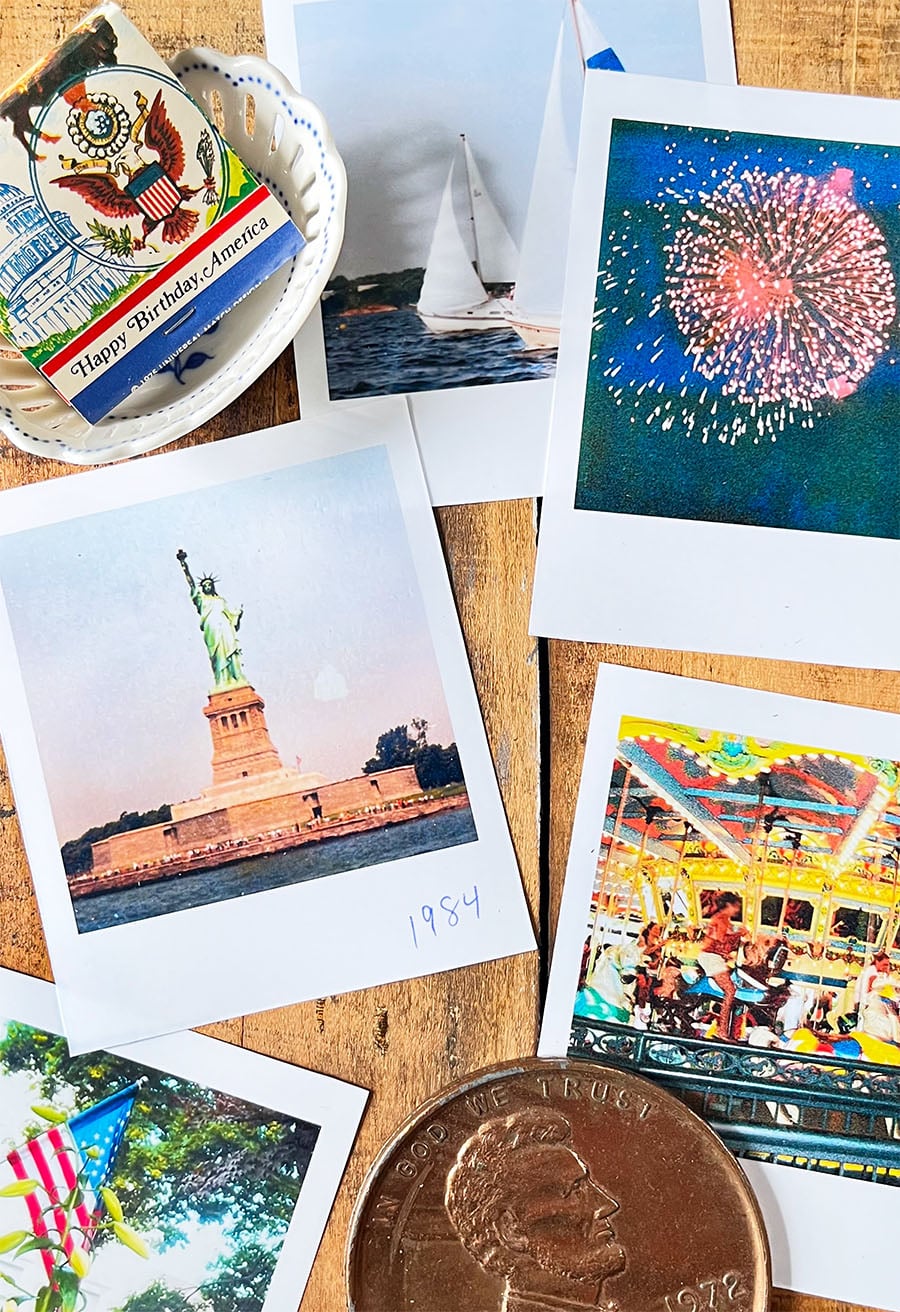 Flatlay of vintage polaroid shots of firewords, sailboats, the statue of Liberty take in 1984 from the harbor, a merry-go-round and the edge of a flag. Top left is a small white dish with a matchbook with an American Eagle and the white house with Happy Birthday America type at the bottom. Bottom right is an oversized souvenir copper penny.