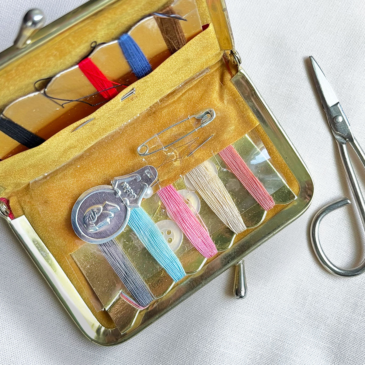 Vintage purse size sewing kit shown open with tiny metal scissors, thread wrapped around gold cards and a golden suede interior.