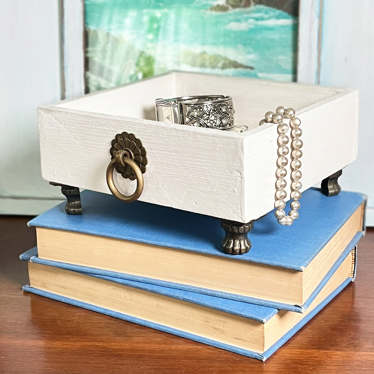 Chic valet tray made from a 6" x 6" rustic wood box/tray found at a thrift store. Small brass feet and brass pull added and the wood box painted white.