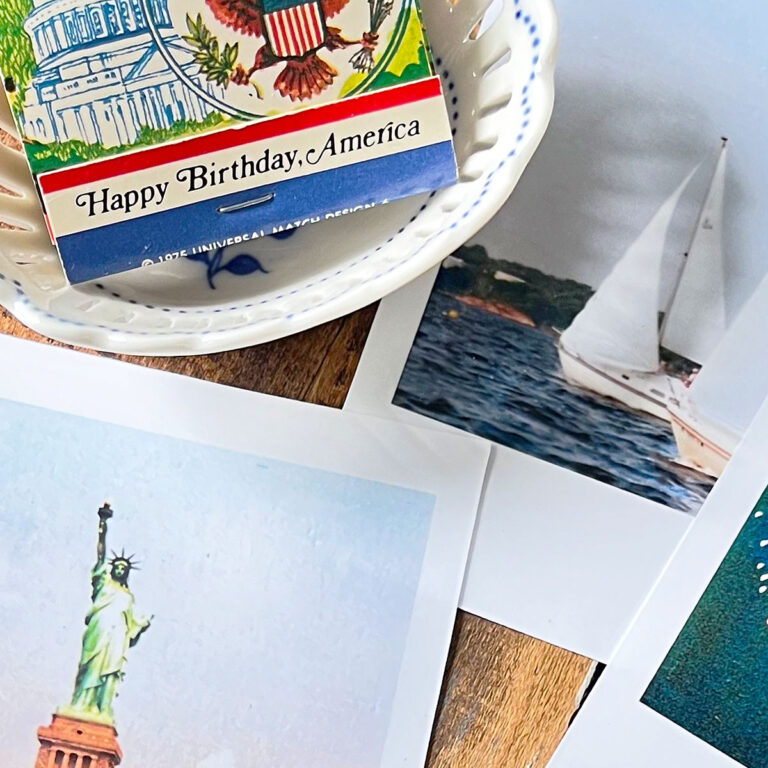 Closeup of vintage patriotic matchbook that says Happy Birthday America with a sailboat photo and a photos of the statue of liberty and a peek of a fireworks photo at the bottom.