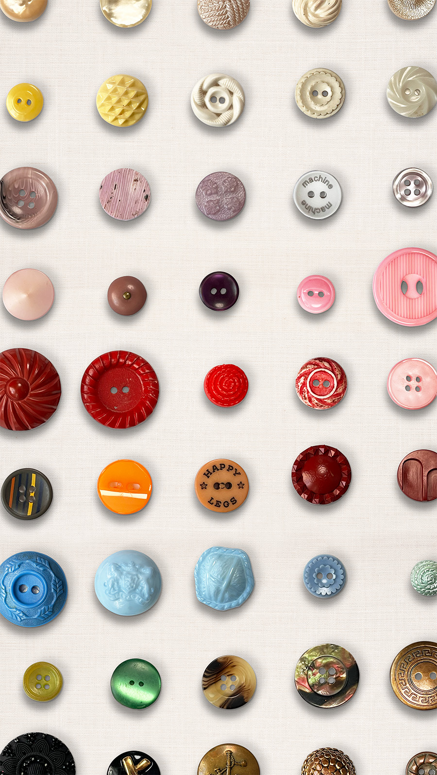 Vertical flatlay grid of 54 vintage buttons five rows and nine columns. The colors go from pearl, butter yellow, light purple, pinks, reads, orange, blue, green, tortoise shell, black and last brass. Each has a unique shape some shank buttons and some with two or four holes.