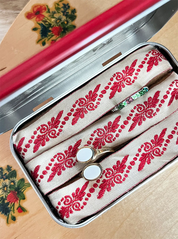 Open Altoids tin transformed into a DIY travel ring holder with fabric-covered ring rolls and two rings inside.