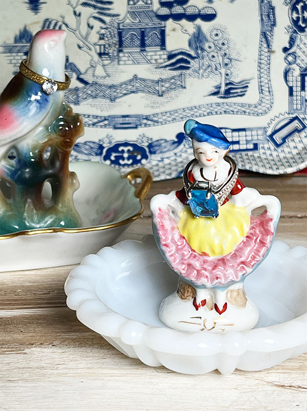 Vintage figurine ring holders made from thrifted butter pat dishes displayed together on a blue transferware tray.