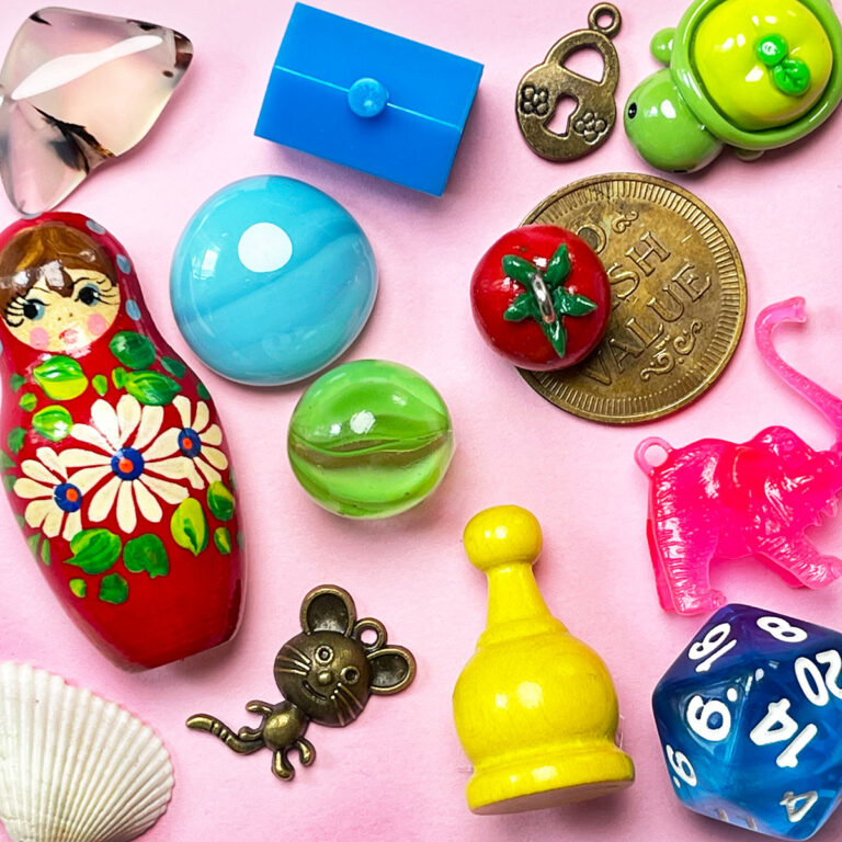 Collectable miniatures on a pink background like coins, nesting doll pin, marbles, game pieces and resin animals.
