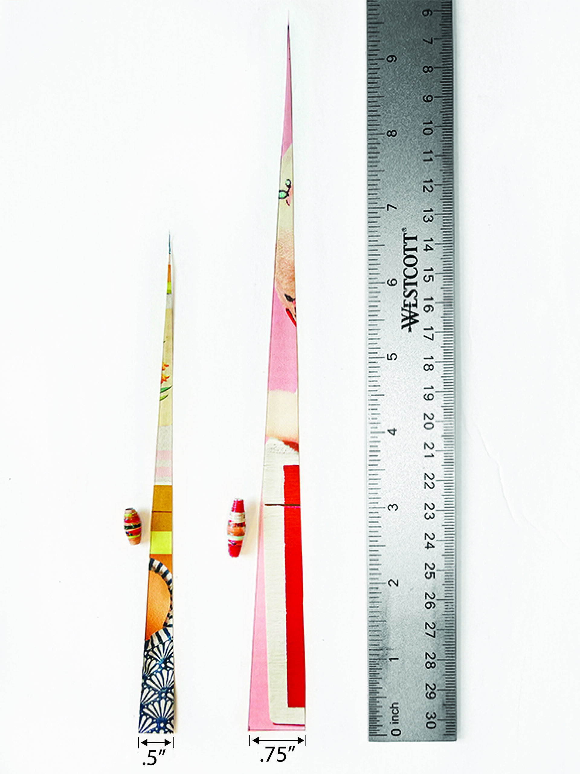Two long paper triangles cut from a glossy colorful magazine page showing dimensions and corresponding bead size once rolled. There is a long bead made from a .75" x 9.75" triangle and a smaller barrel sized bead that is make from a .5" x 6.75" triangle of paper. Ruler also at the bottom from reference.