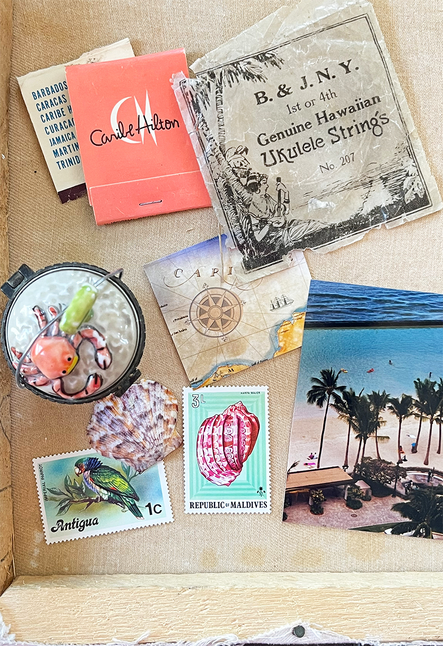 A tropical-inspired collage arranged on a stretched canvas featuring vintage Hawaiian ukulele string packaging, a Coral Hilton matchbook, Caribbean map ephemera, colorful postage stamps, seashells, a beach photograph with palm trees, and a small crab ornament, creating a collection of travel memories and seaside keepsakes.
