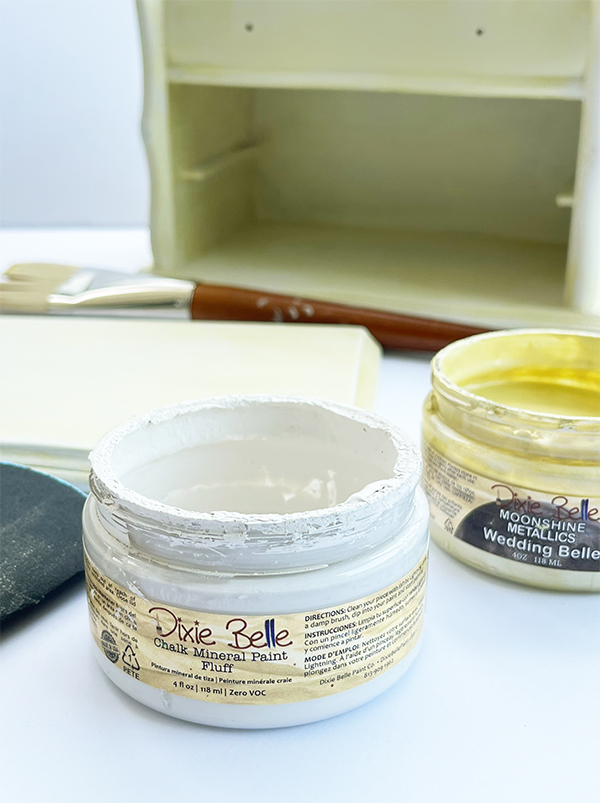 Dixie Belle Fluff chalk mineral paint, Wedding Belle metallic paint, and sandpaper used to create a soft champagne finish to comlete a thrift store jewelry box makeover.