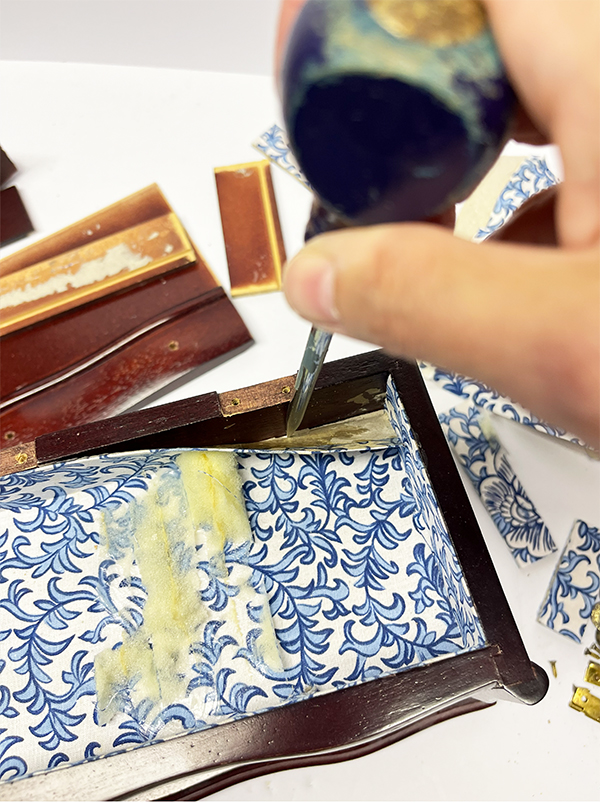 Removing the original fabric-lined cardboard insert from small drawers with an awl for a thrift store jewelry box makeover.