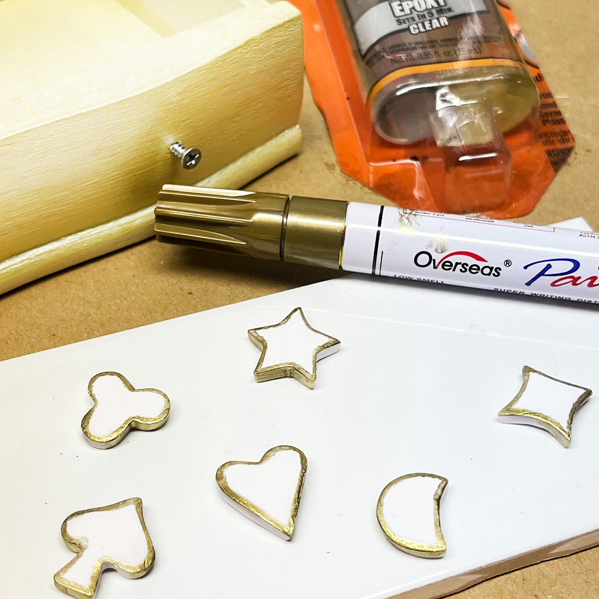 Photo of making handmade lucky charm shaped knobs, stars, clovers, spade, heart, moon shapes made from polymer clay, baked and then adding gold edging with a oil based acrylic gold pen for a thrift store jewelry box makeover.