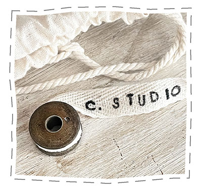 Colophon at the end of the Vintage Button Tins Find and Handmade Ideas post that has a vintage bobbin with a woven ivory cotton ribbon unwinding, stamped C. STUDIO.
