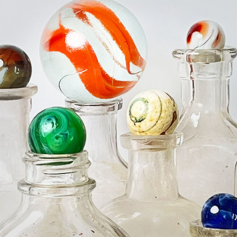 Closeup of a collection of colorful marbles of varying sizes set on top of empty vintage clear bottles.