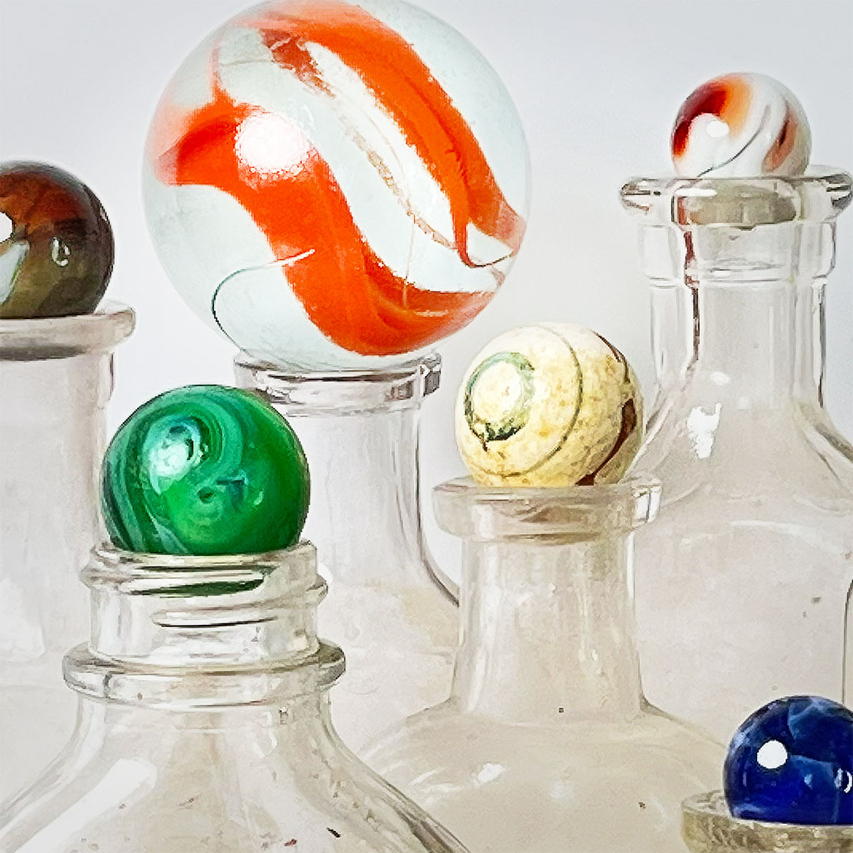 Closeup of a collection of colorful marbles of varying sizes set on top of empty vintage clear bottles.