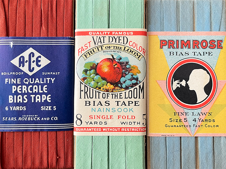 Three vintage bias tape packages in red, mint green, and blue-gray, featuring colorful A&E, Fruit of the Loom, and Primrose paper labels.