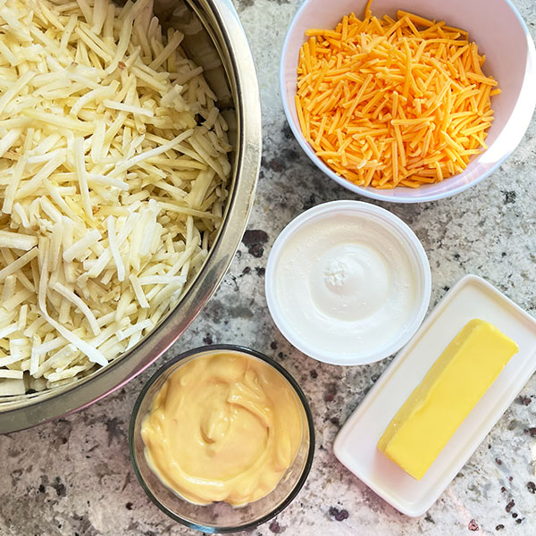Ingredients to make Baked Cheesy Hash Brown Potatoes: Hashbrown potatoes, shredded sharp cheddar, sour cream, cream of chicken and 1/2 cup butter.